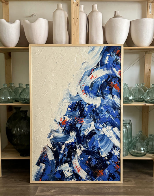 A contemporary art piece with a vibrant mix of blue and orange, acrylic paint on wood, displayed in a home setting with various decorative objects in the background.